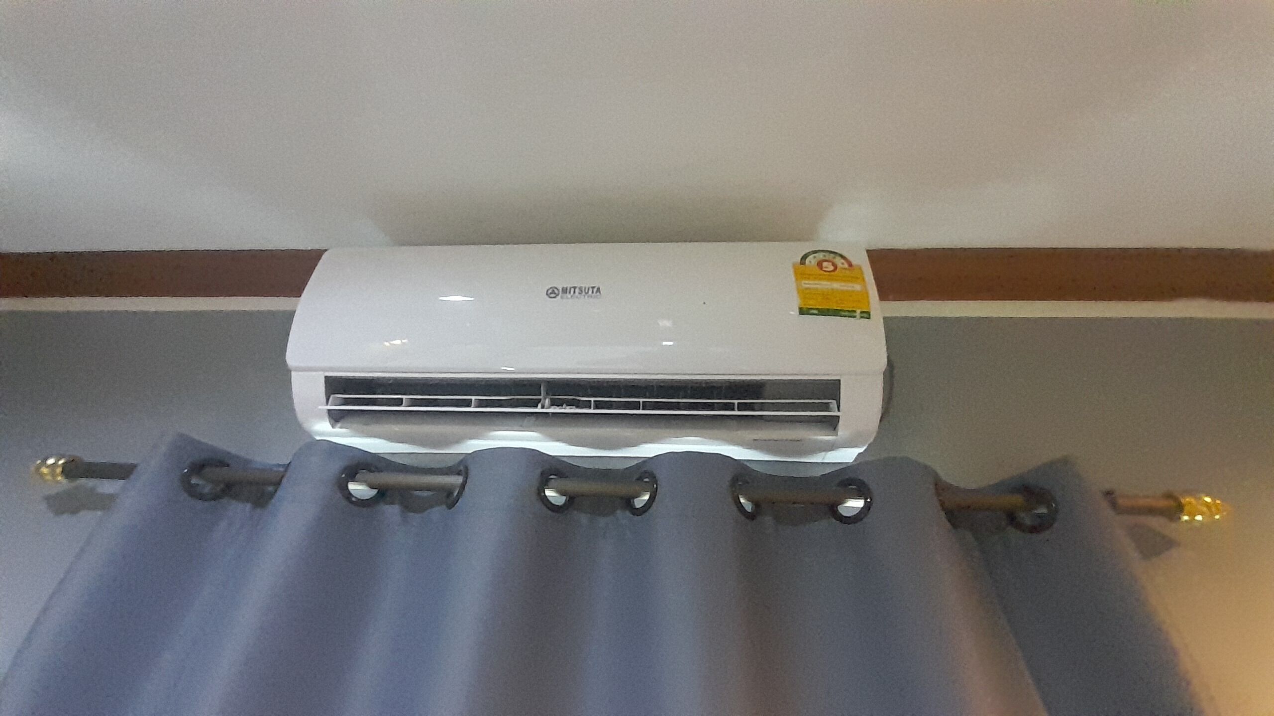A white air conditioning unit mounted on a wall with a metal bracket and a grey curtain below it.