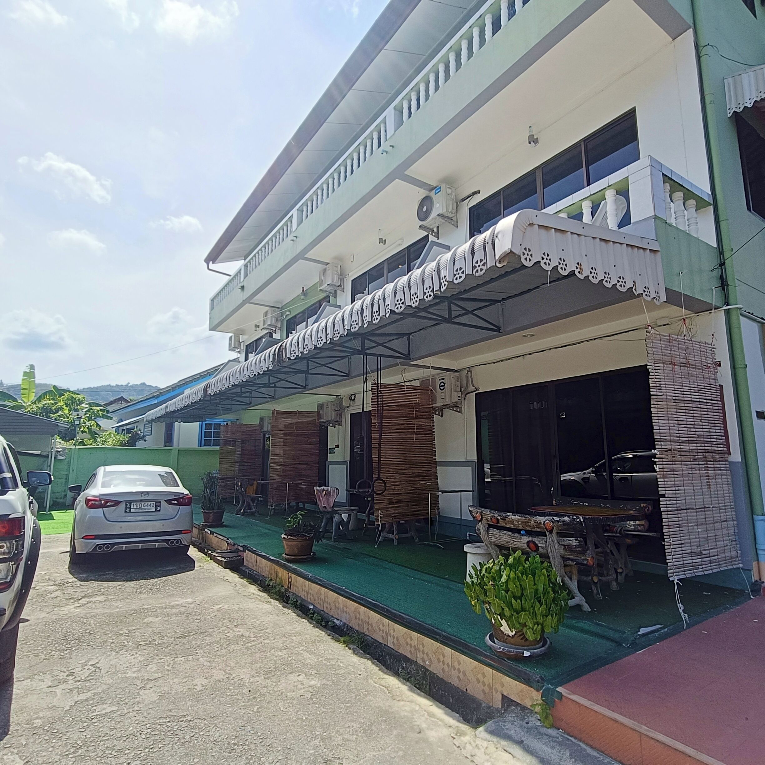 A two-story building with a covered porch, a car parked in front, and potted plants.