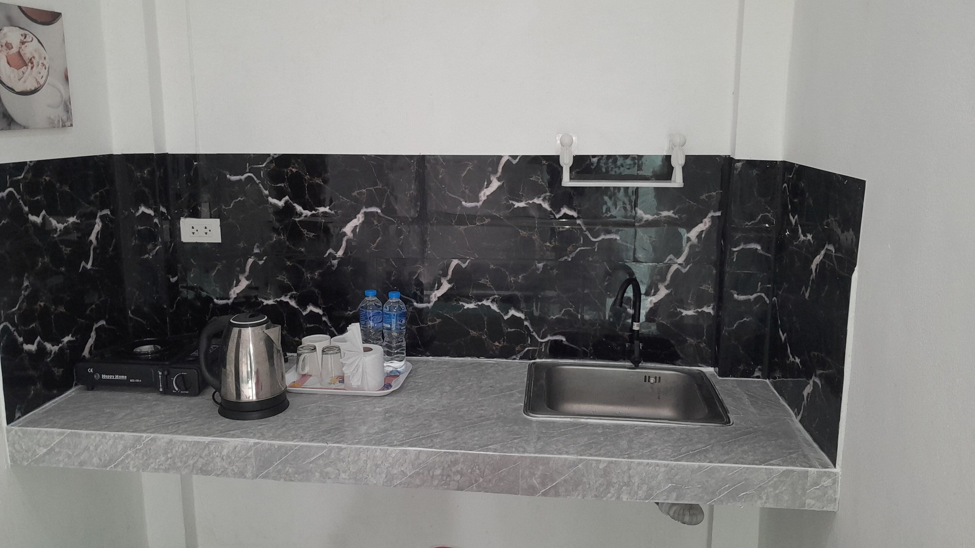 A kitchen with a black marble backsplash, a stainless steel sink, a kettle, and a water dispenser.