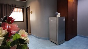 A compact kitchen with a refrigerator, a wooden cabinet, and a window with curtains. - The Guest House  (Patong)