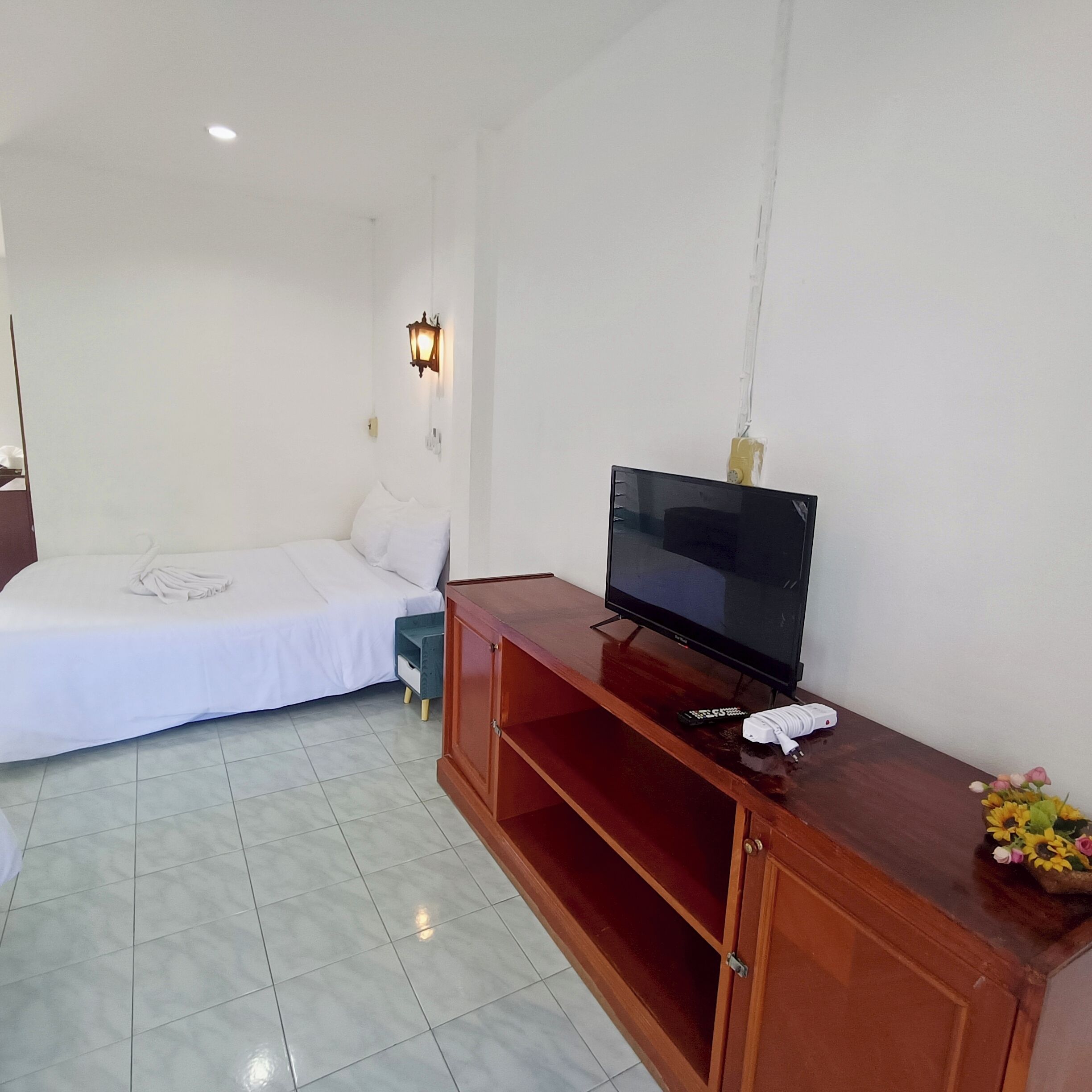 A hotel room with a bed, a TV on a wooden stand, and a small table with a vase of flowers.