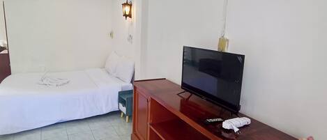 A hotel room with a bed, a TV on a wooden stand, and a small table with a vase of flowers.