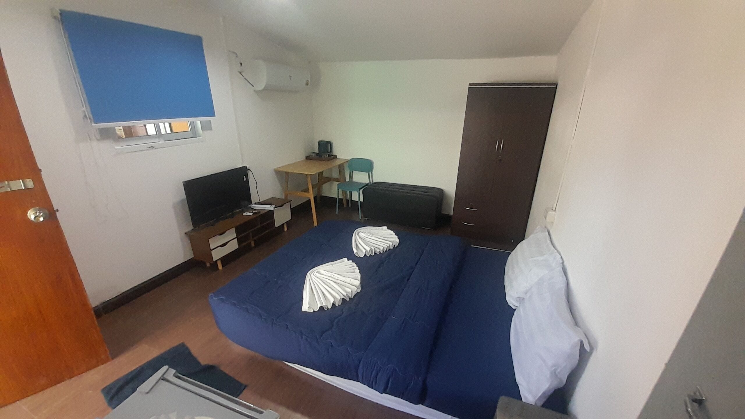 A hotel room with a bed, a desk, a chair, a wardrobe, and a television.