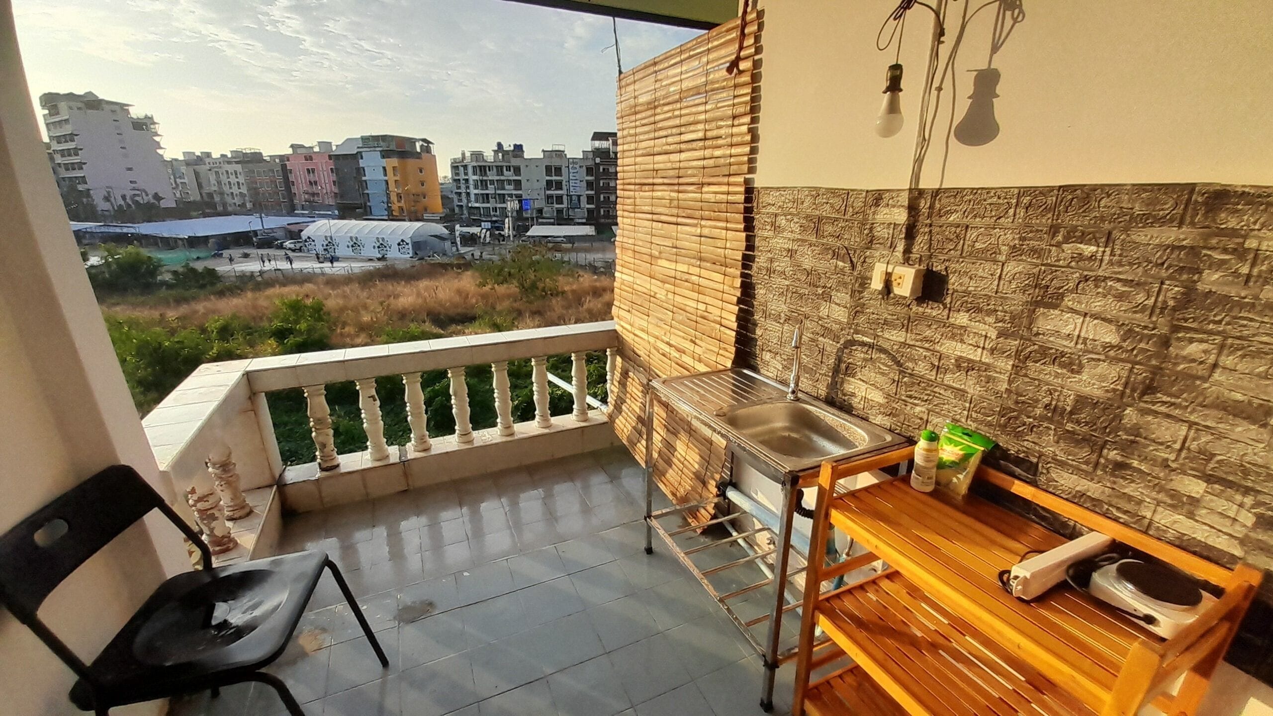 En balkon med vask, stol og bord, der udover et bybillede med bygninger.