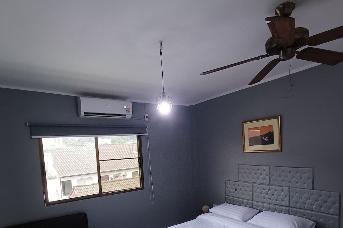 A bedroom with a bed, a ceiling fan, a window, and an air conditioning unit.