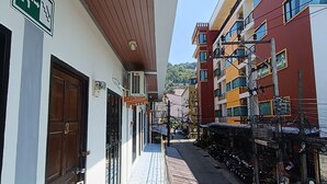 A narrow alleyway with buildings on either side, a visible emergency exit sign, and a clear sky. - The Guest House  (Patong)