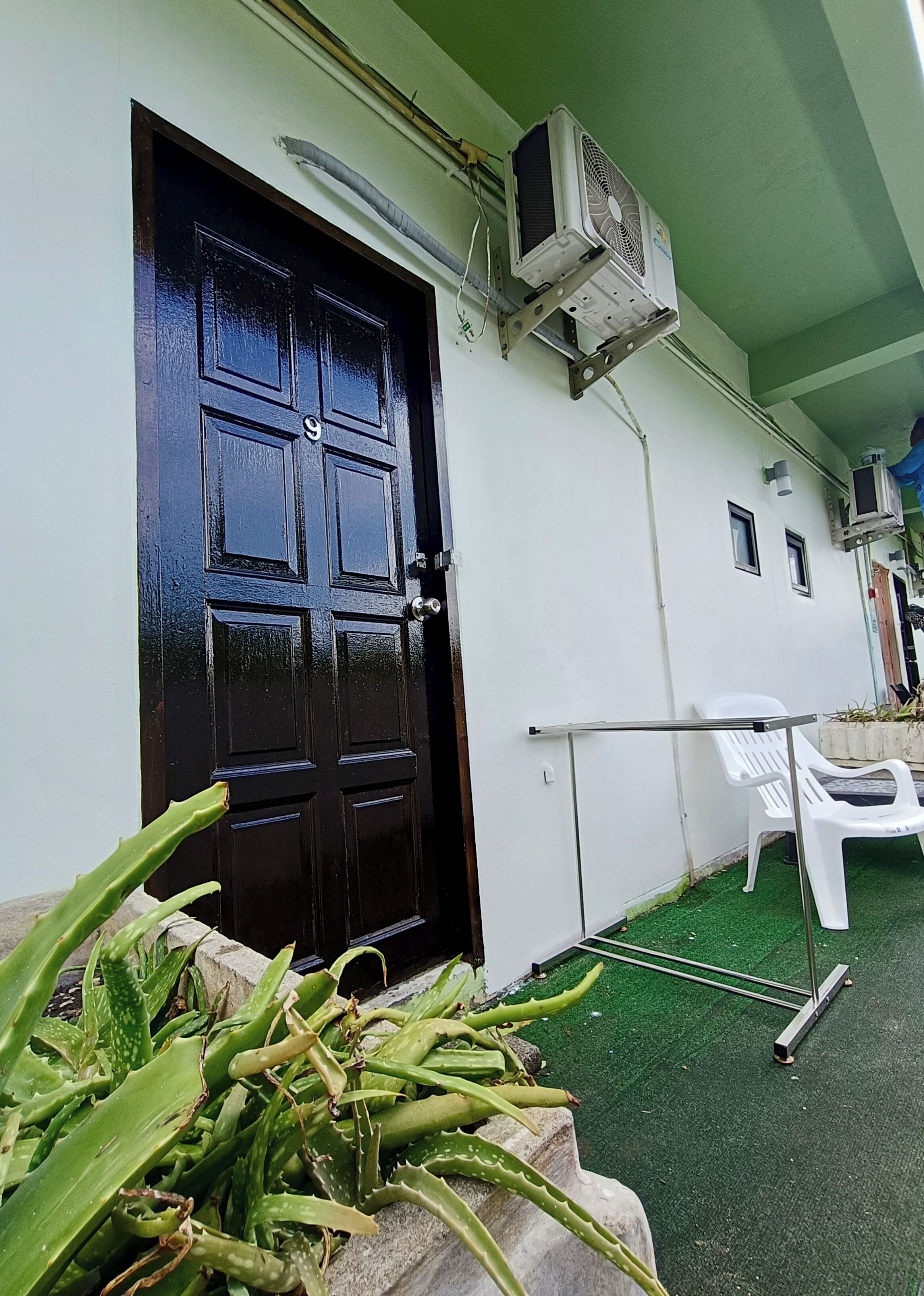 A building with a black door, an air conditioning unit mounted on the wall, and a white chair outside.