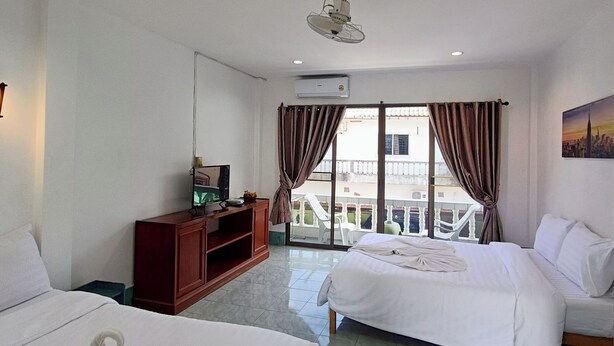 A hotel room with two beds, a TV on a wooden cabinet, an air conditioner, and a balcony with curtains. - The Guest House  (Patong)