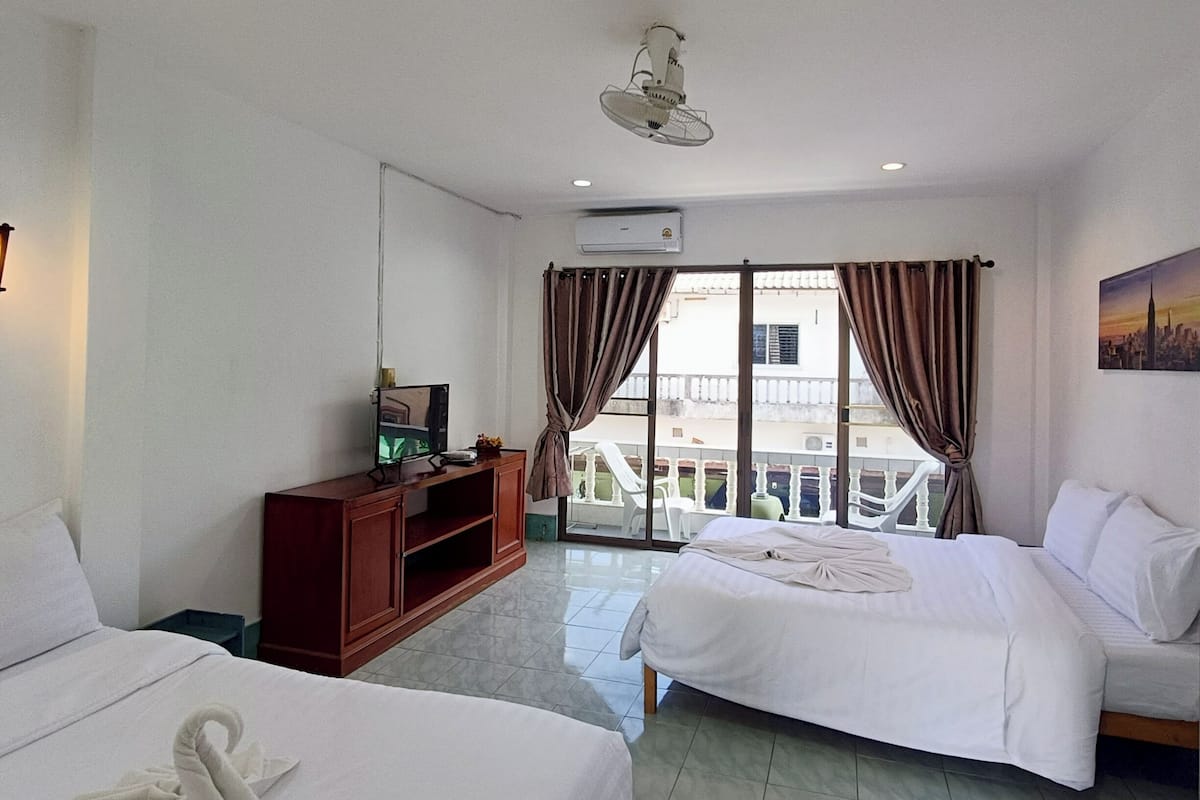 A hotel room with two beds, a TV, a wooden cabinet, and a balcony with a view of the city.