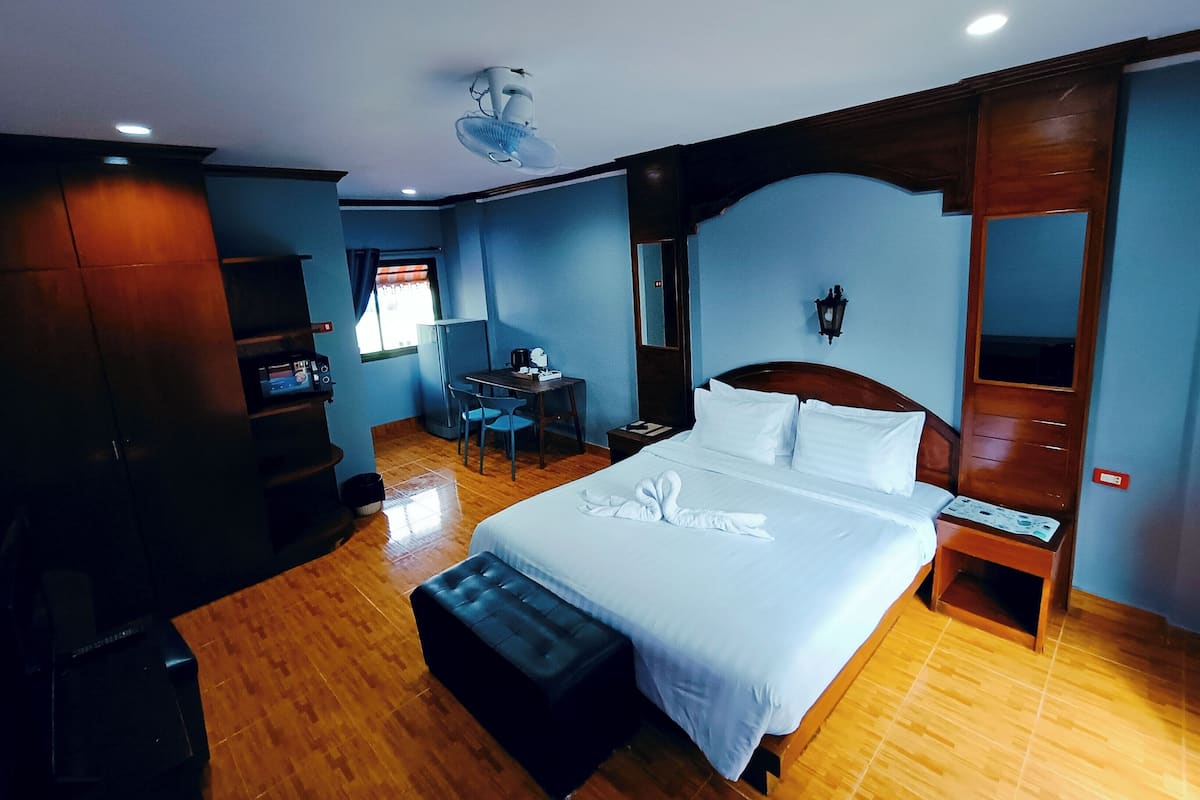 A hotel room with a bed, a desk, a chair, a small table, a mirror, and a ceiling fan.