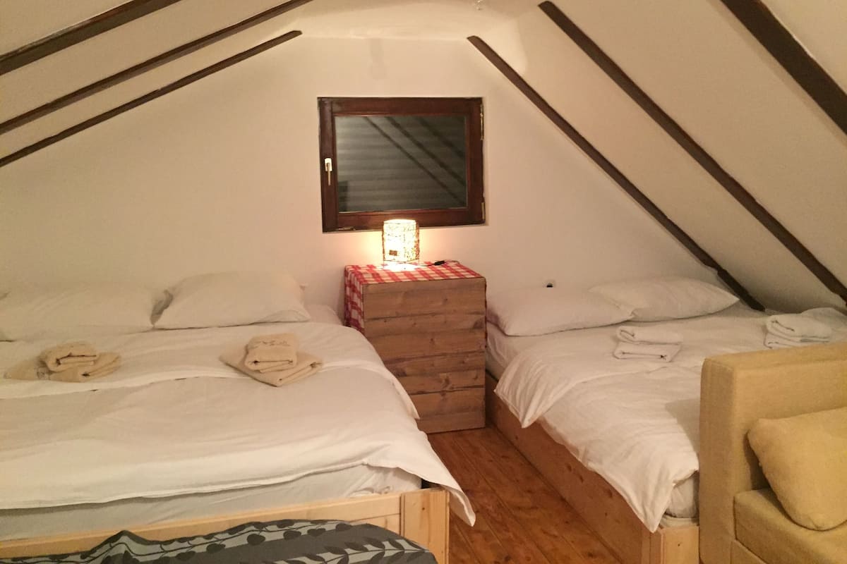 Une petite chambre accueillante, avec deux lits, une commode en bois et une table de chevet avec une lampe.