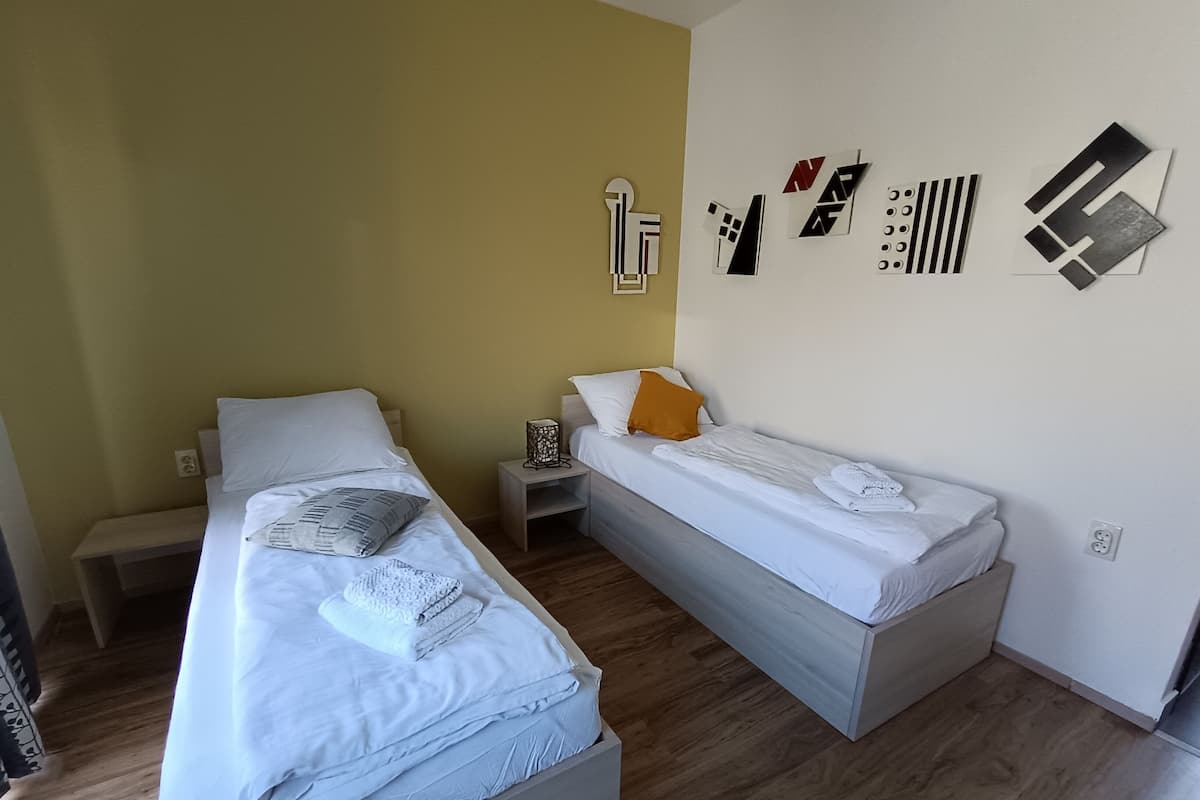 Une chambre avec deux lits, une table de chevet avec une lampe et un mur orné d’œuvres d’art abstraites.