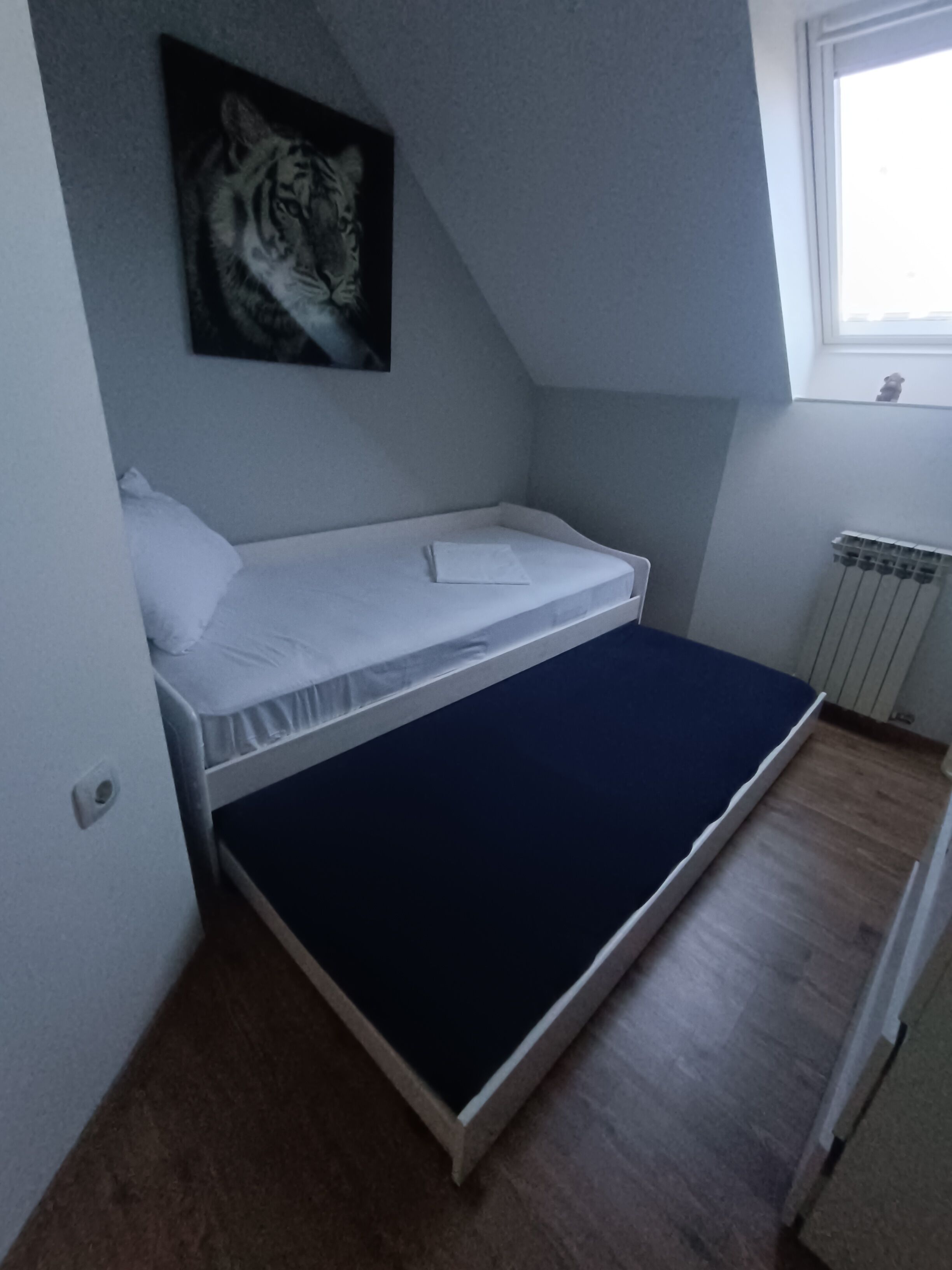 A small, single-bed room with a sloped ceiling, a radiator, and a window.