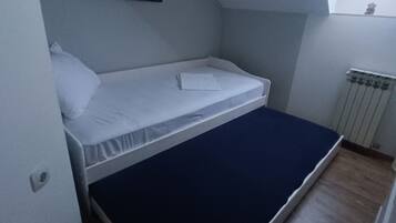 A small, single-bed room with a sloped ceiling, a radiator, and a window.