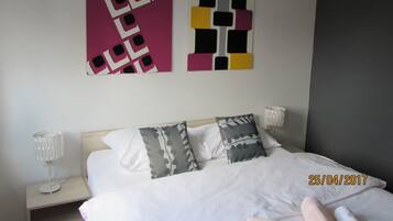 A hotel room with a bed, two pillows, a nightstand with a lamp, and two wall art pieces.