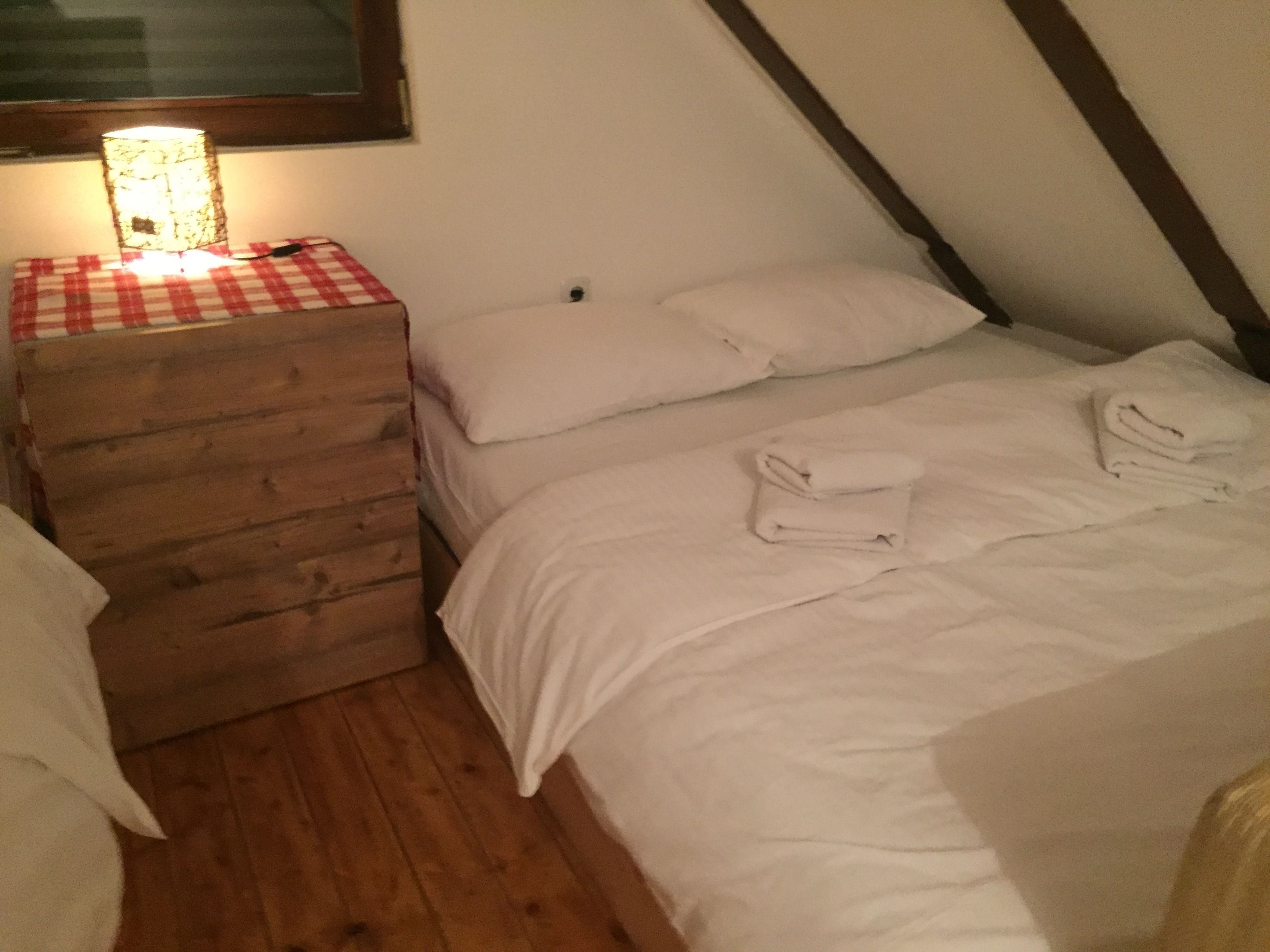 Un dormitorio con un aparador de madera, una cama con ropa blanca y una lámpara sobre el aparador.