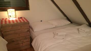 Un dormitorio con un aparador de madera, una cama con ropa blanca y una lámpara sobre el aparador.