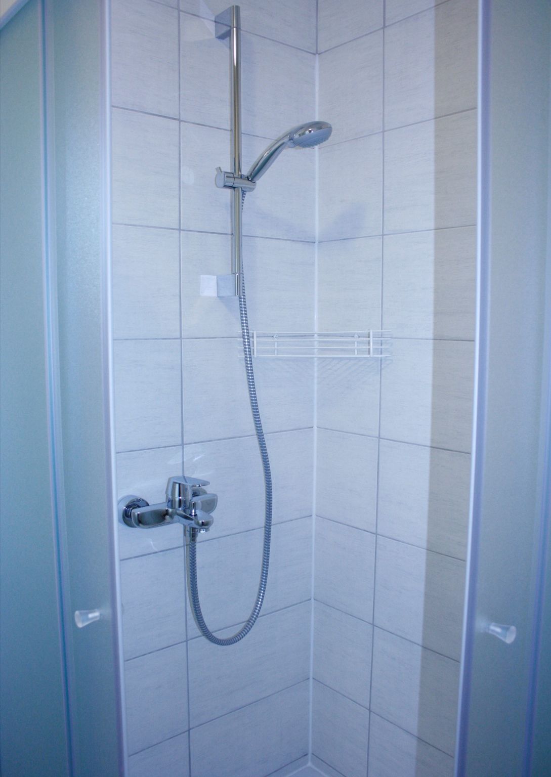 A shower with a handheld showerhead and a fixed showerhead, both mounted on a wall.