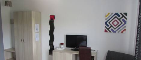 Una habitación pequeña y moderna con un armario de madera, un escritorio con una computadora, una silla y un adorno en la pared.