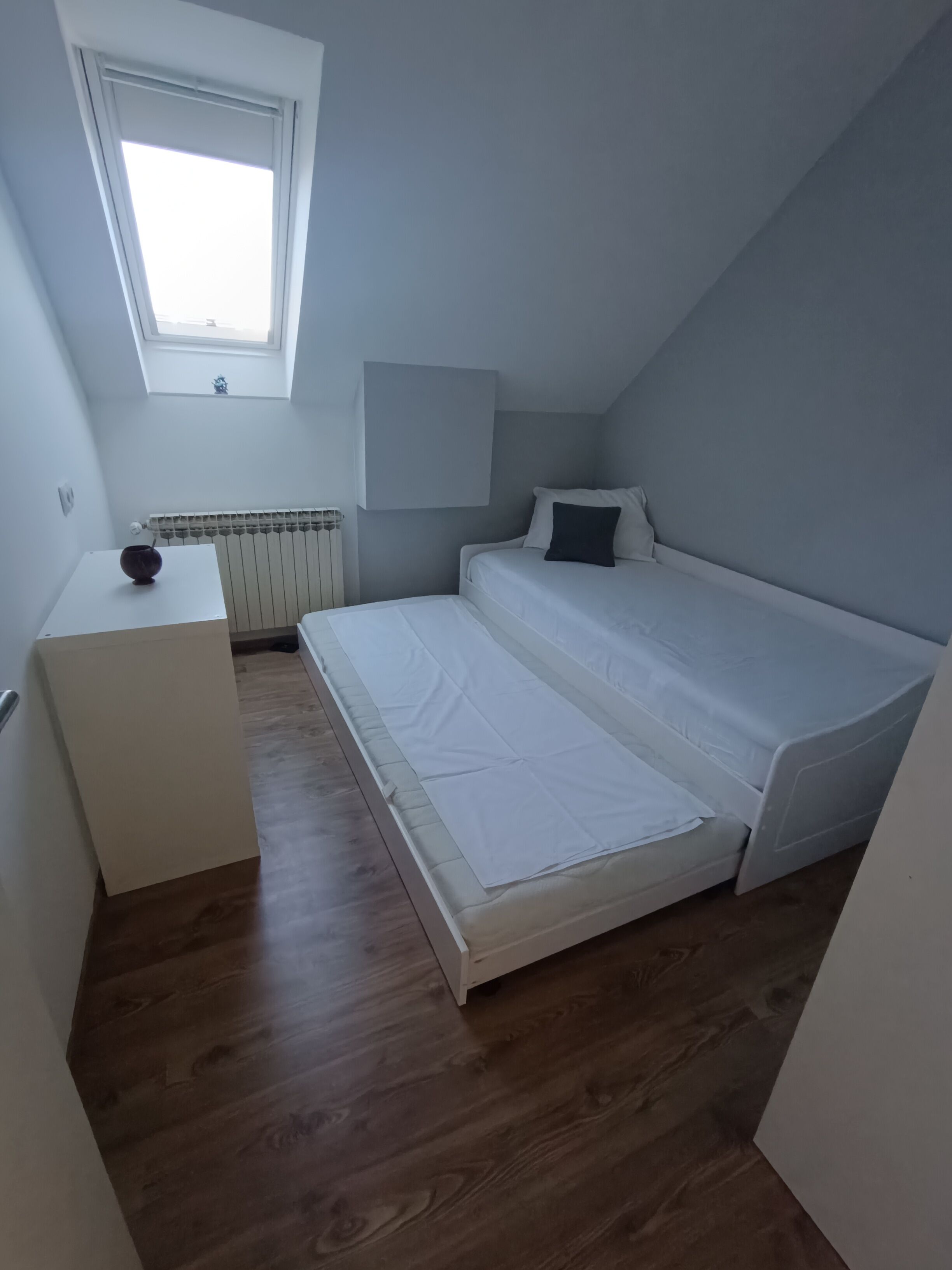 A small, single-bed room with a skylight, a radiator, and a bedside table.