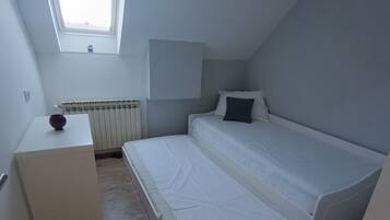 A small, single-bed room with a skylight, a radiator, and a bedside table.