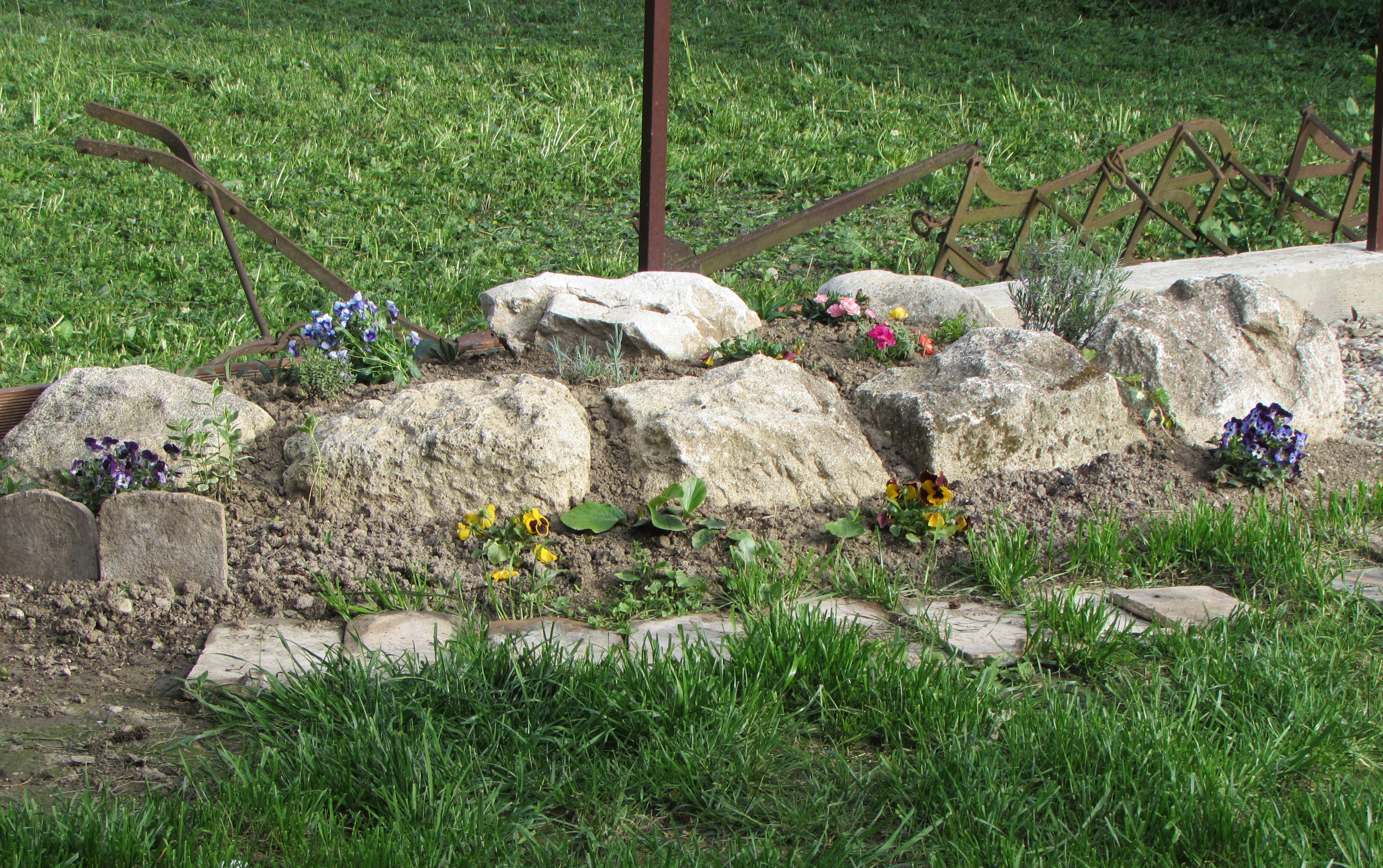 Un jardín con rocas grandes, flores y una cerca de metal.