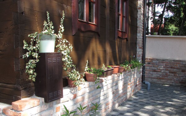 Un edificio de madera con base de ladrillo, plantas en macetas y un cuadro eléctrico de metal.