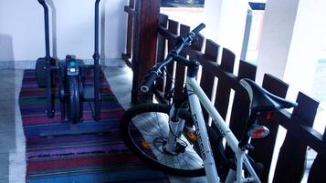 A room with a wooden ceiling, a colorful striped rug, a white bicycle, and two exercise bikes.