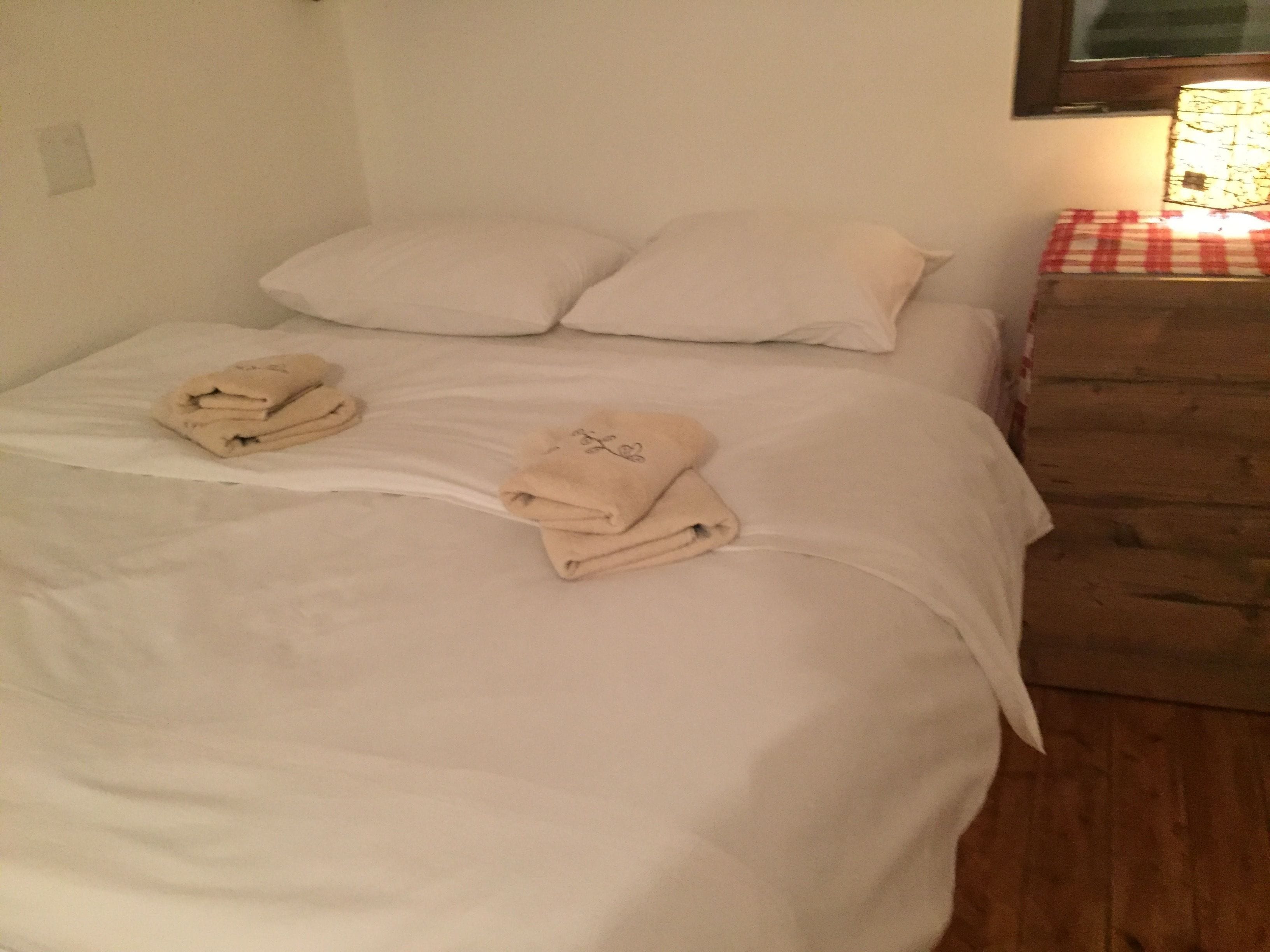 Una cama bien hecha con dos almohadas y dos toallas dobladas.