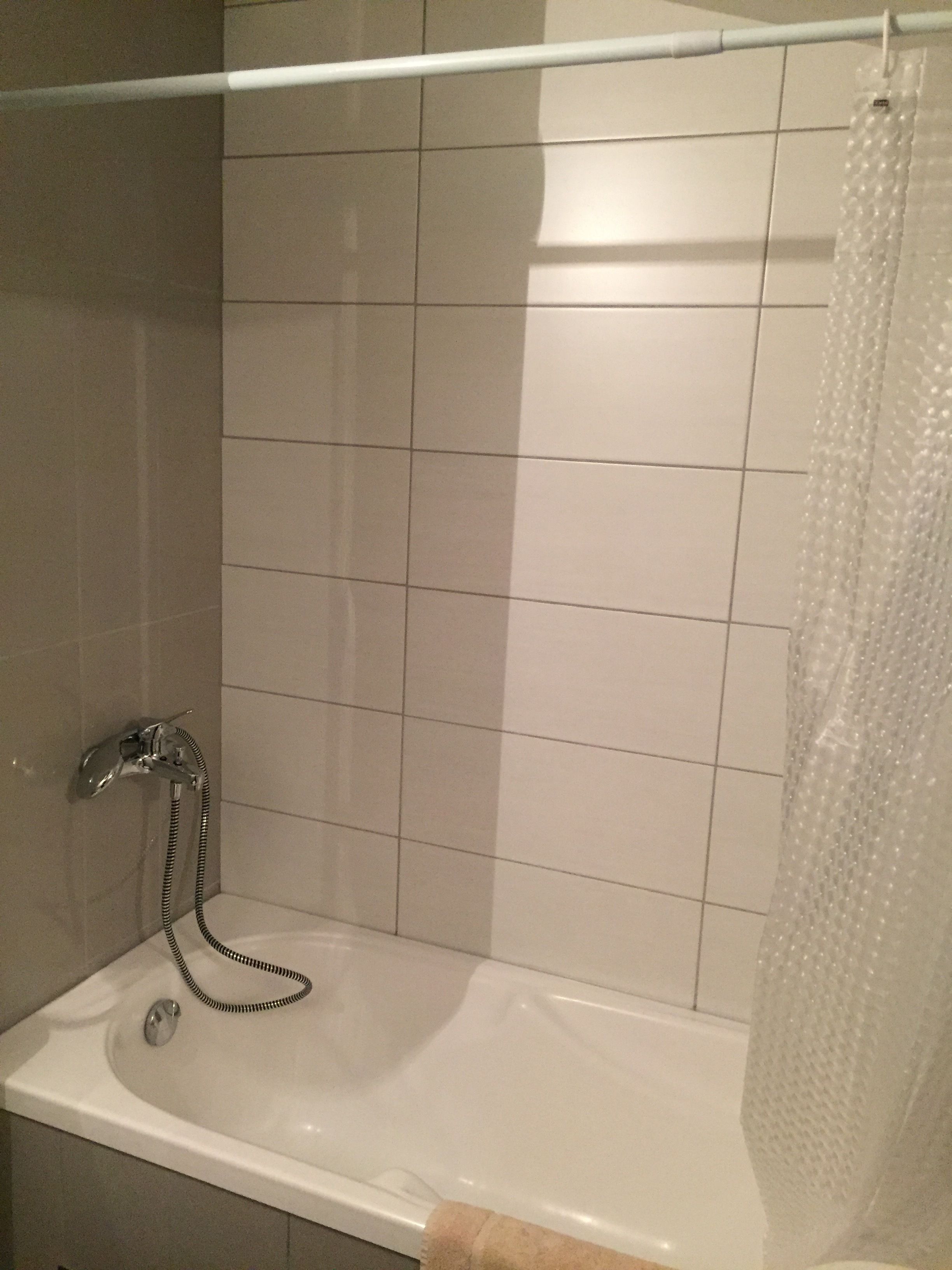 A bathroom with a bathtub, a shower curtain, and tiled walls.