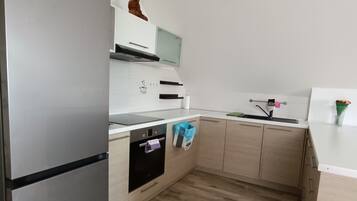 A modern kitchen with a stainless steel refrigerator, a built-in oven, and a microwave. There is a wooden floor and light-colored cabinetry.