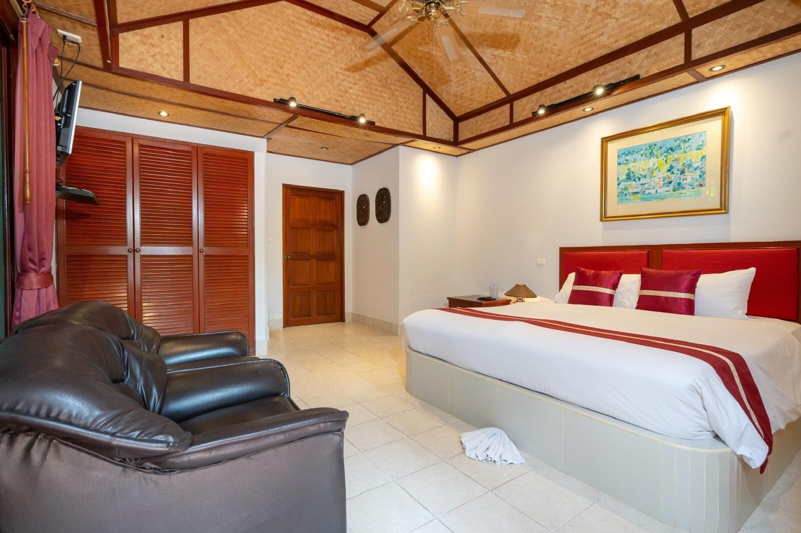 Une chambre d’hôtel avec un lit, un canapé, un ventilateur de plafond, une porte en bois et un tableau au mur.
