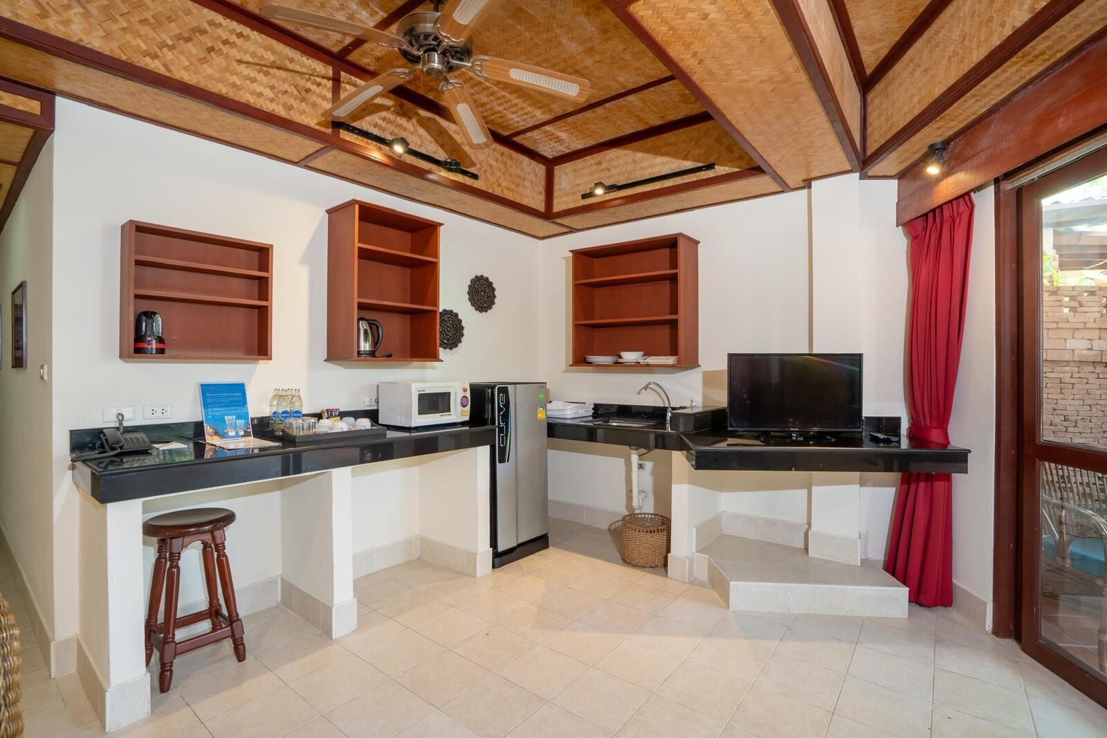 A compact kitchen with a built-in refrigerator, microwave, and stove. There are wooden cabinets and a ceiling fan.