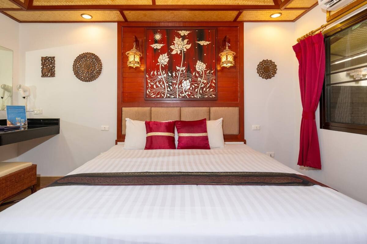 Une chambre d’hôtel avec un grand lit, une tête de lit en bois, des panneaux décoratifs sur les murs, deux lanternes fixées au mur et une fenêtre avec des rideaux rouges.
