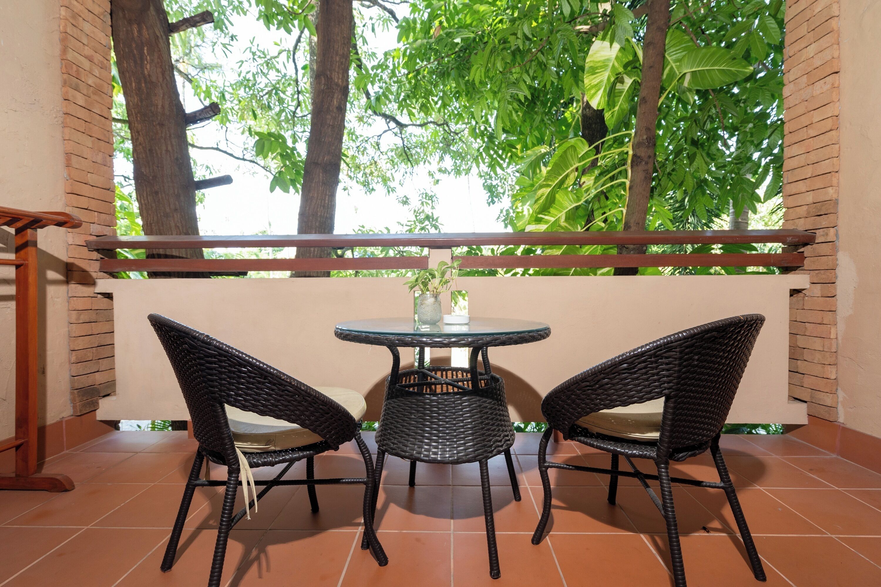 Un balcon agrémenté de deux fauteuils en osier et d’une petite table ronde, donnant sur un jardin luxuriant et verdoyant.