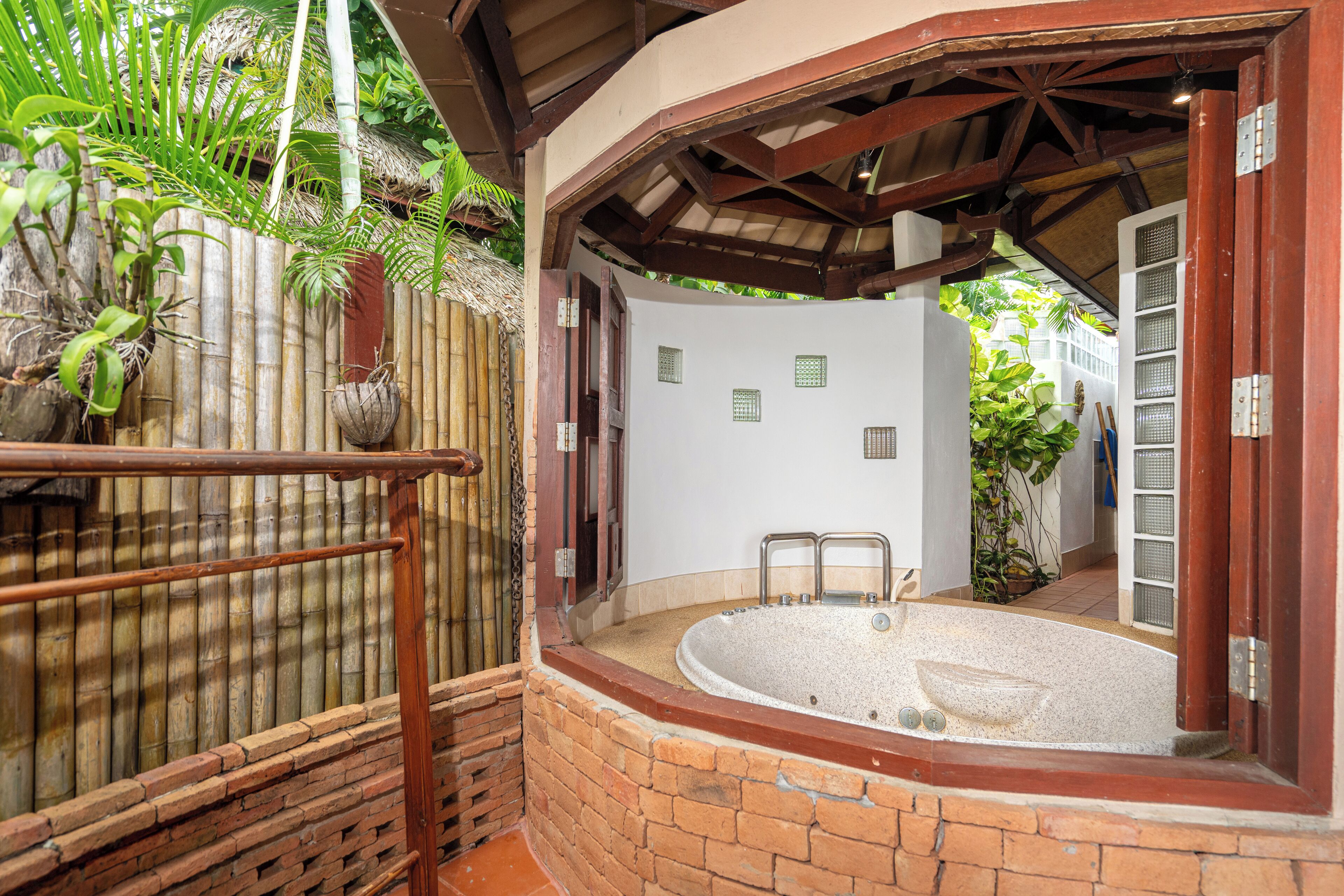 Uma área de spa com banheira de hidromassagem, cerca de bambu e parede de tijolos.