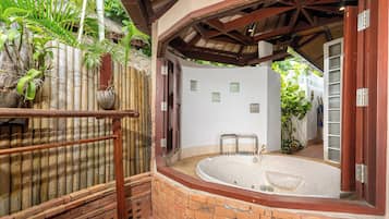 Zona de spa con un jacuzzi, valla de bambú y pared de ladrillo.
