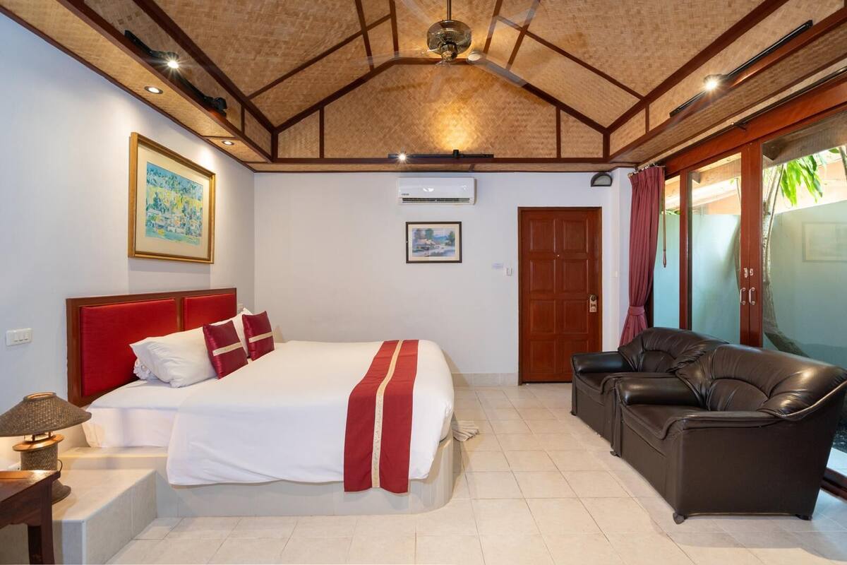 Une chambre d’hôtel avec un lit, un canapé en cuir, un ventilateur de plafond et une porte donnant sur un balcon.
