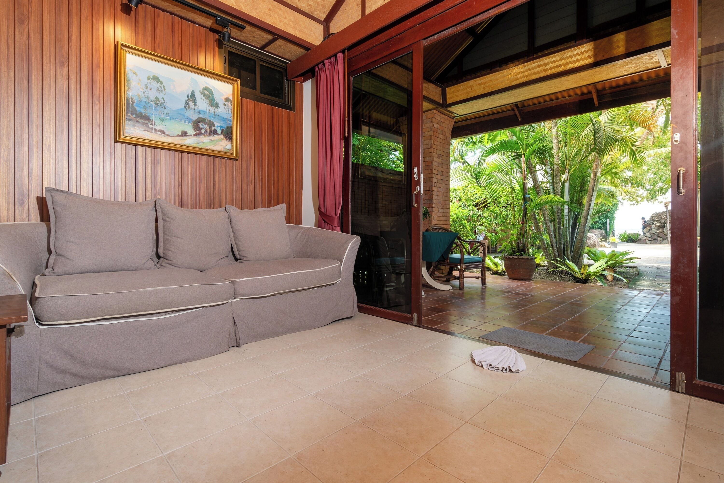 Una habitación con sofá color beige, un cuadro en la pared y vista a un jardín a través de un ventanal.