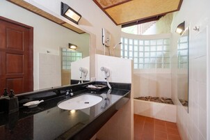 Un baño moderno con encimera negra, lavabo blanco, un espejo grande y una zona de ducha con vistas al exterior.