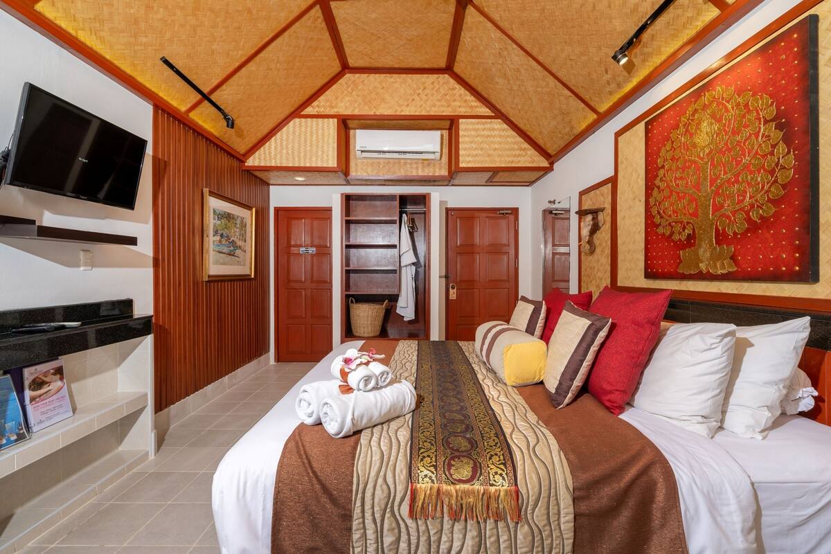Une chambre d’hôtel avec un grand lit, un téléviseur à écran plat, un ventilateur de plafond et un tableau représentant un arbre.