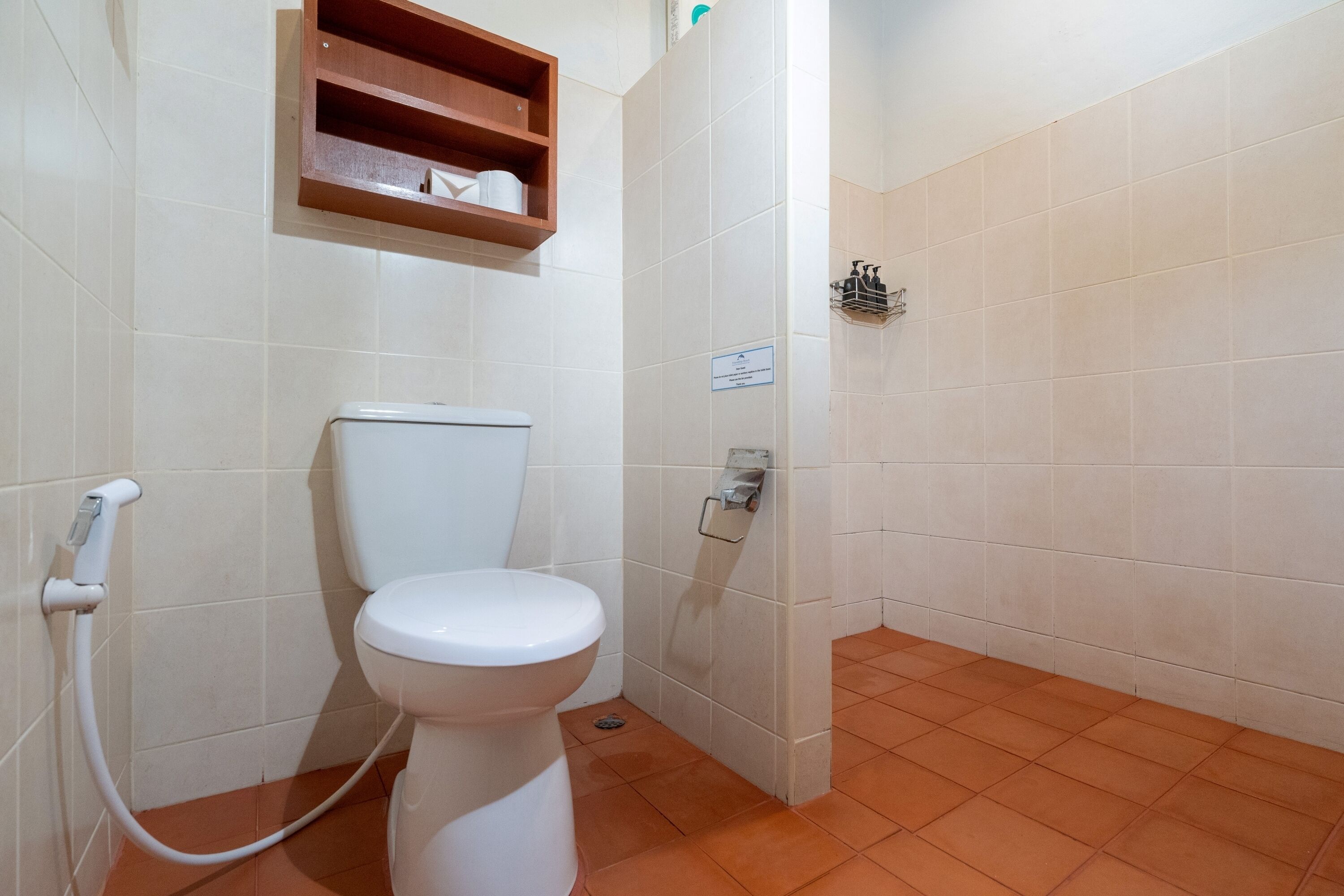 Un baño con inodoro, un estante de madera encima y suelo de baldosas.