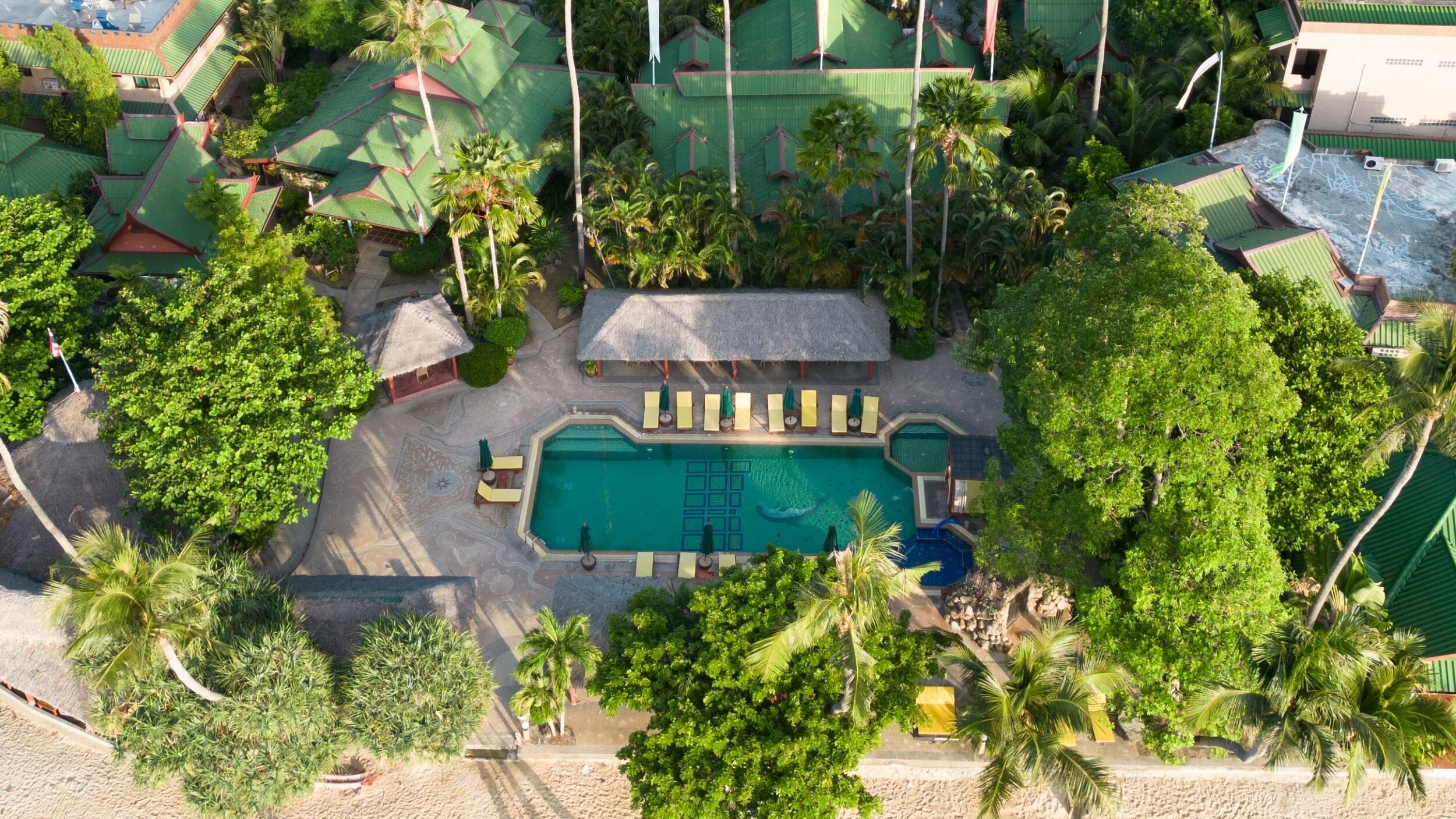 Una vista aerea di un resort con una piscina centrale, circondata da palme e zone relax.