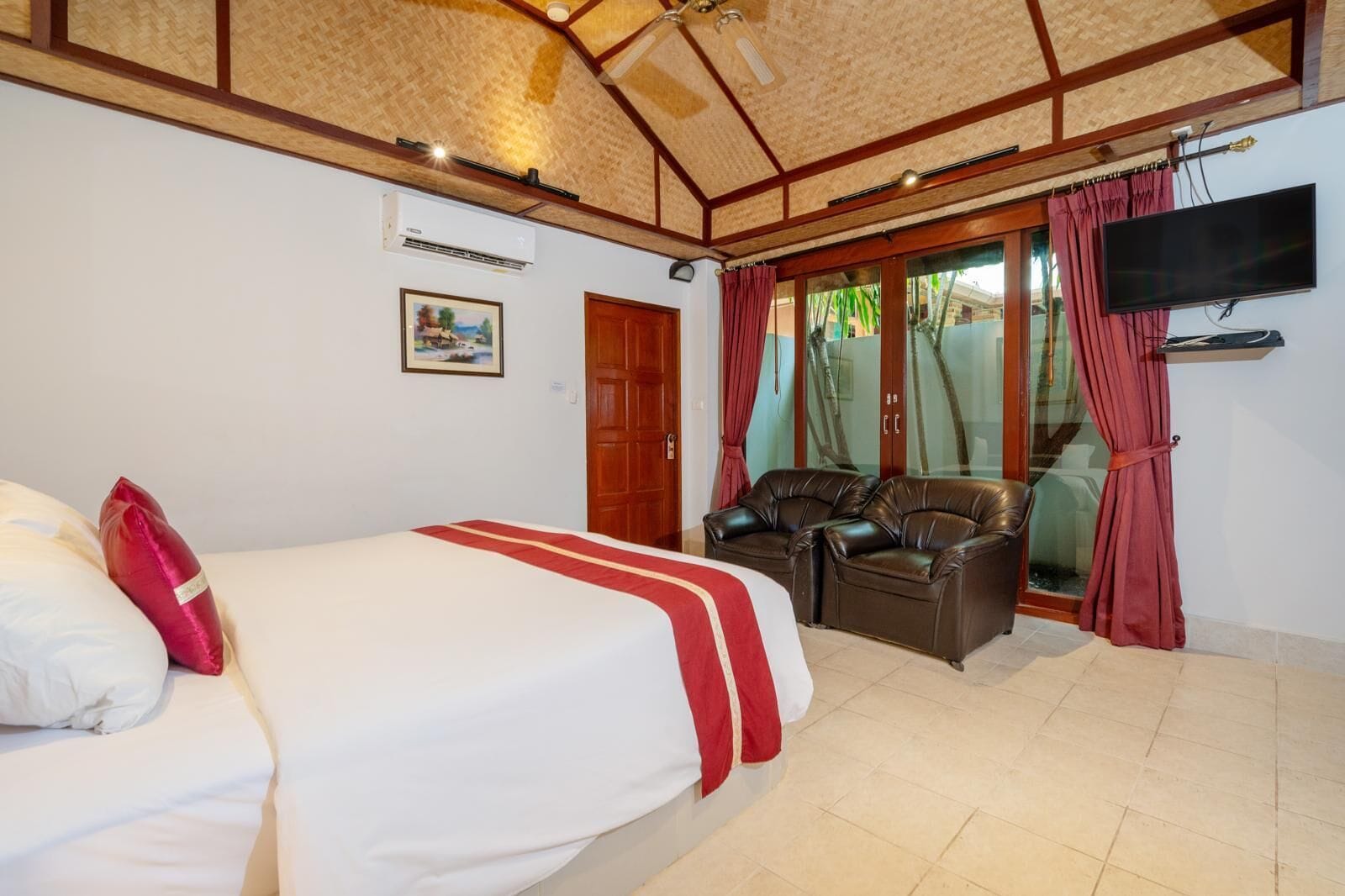 A hotel room with a bed, a TV, a seating area with leather chairs, and a sliding glass door to the outside.