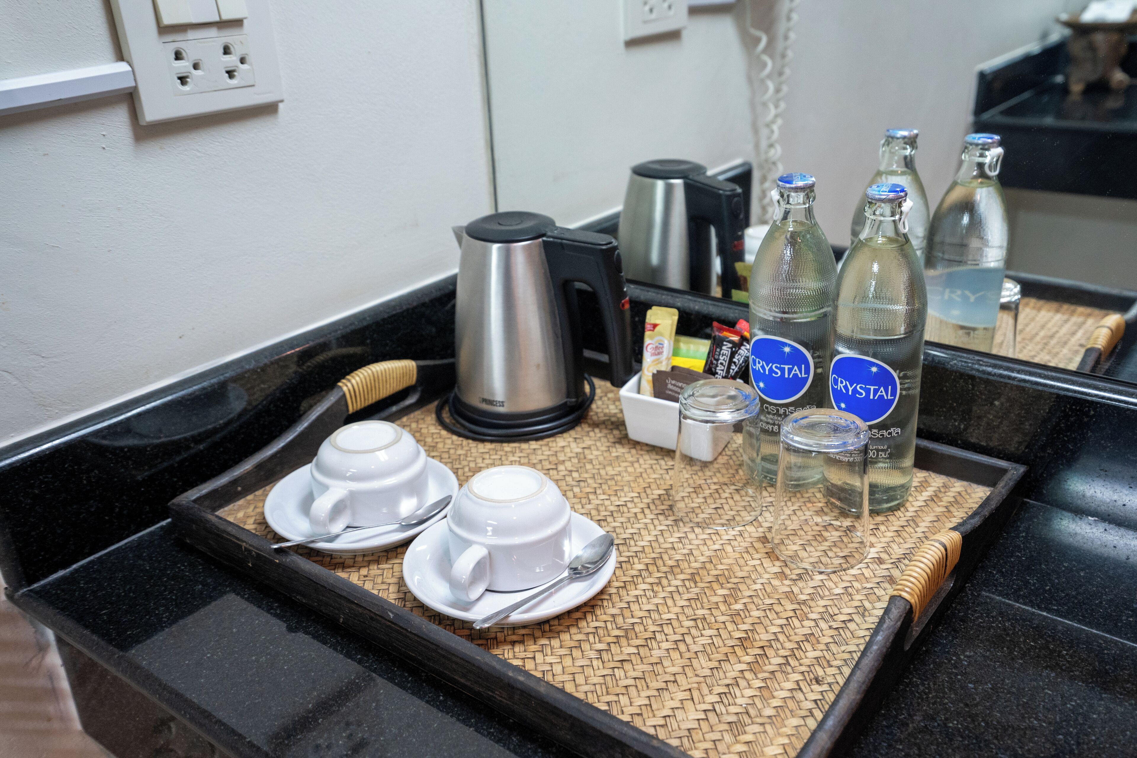 En køkkenbordplade med en kaffemaskine, to hvide kopper, en ske og flasker mærket "Crystal".