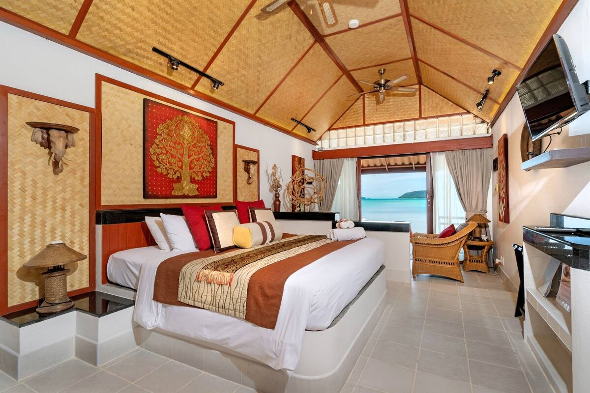 Une chambre spacieuse avec un grand lit, un ventilateur de plafond et une vue sur la mer.