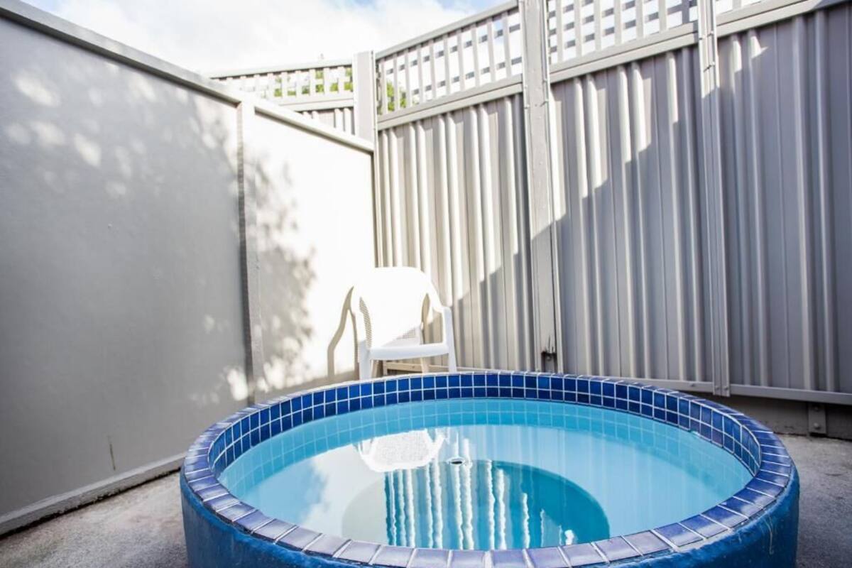 A small, round hot tub with a tiled edge, surrounded by a white fence and a concrete floor.