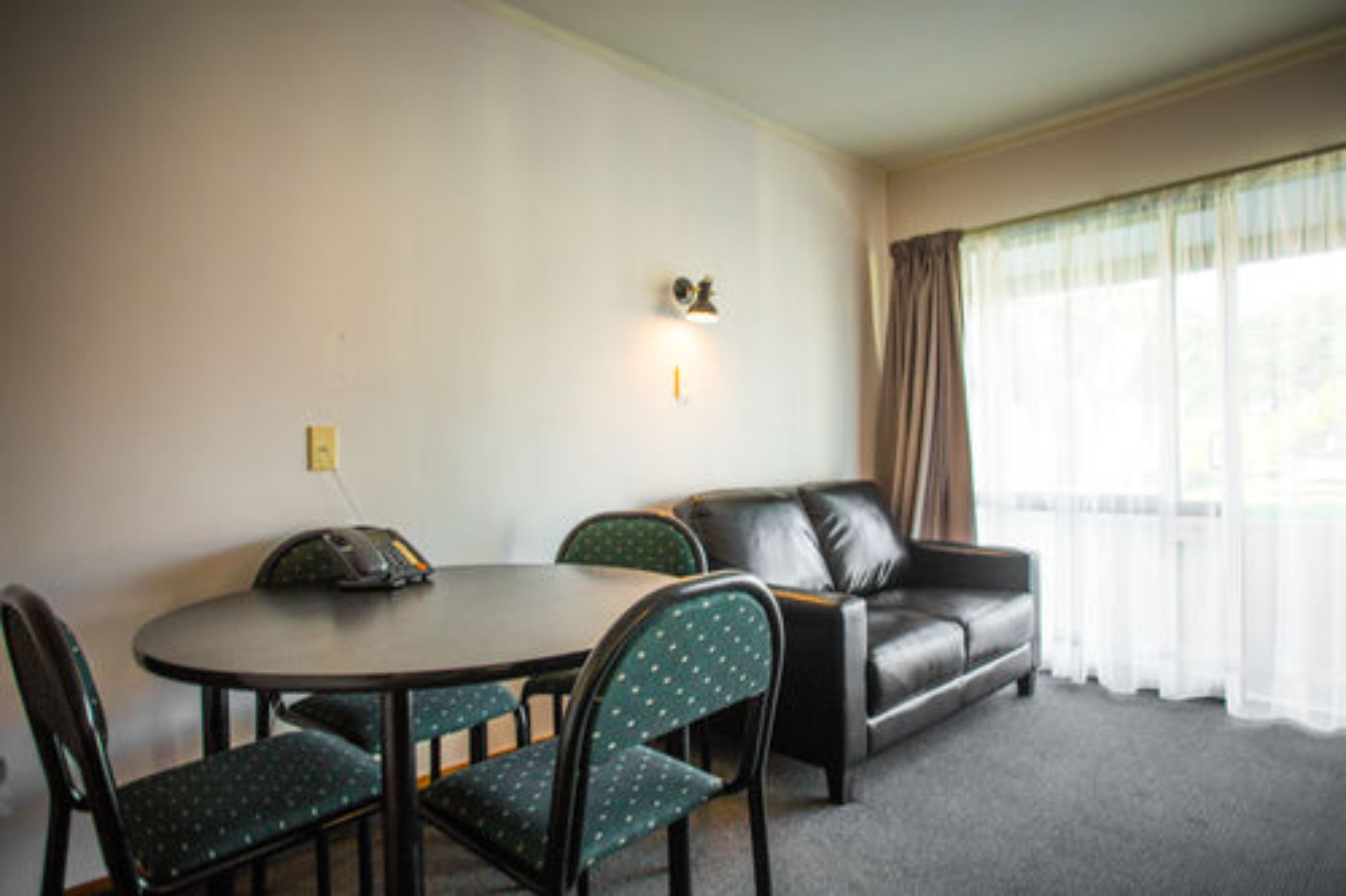 A room with a round table, four chairs, a sofa, and a window with sheer curtains.
