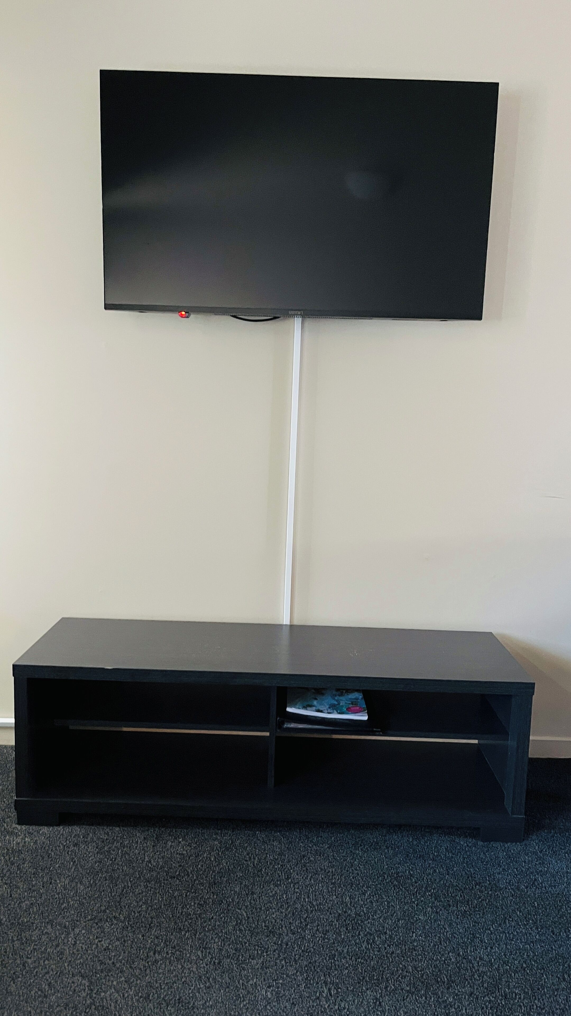 A flat-screen TV mounted on a white wall with a black entertainment unit below it.