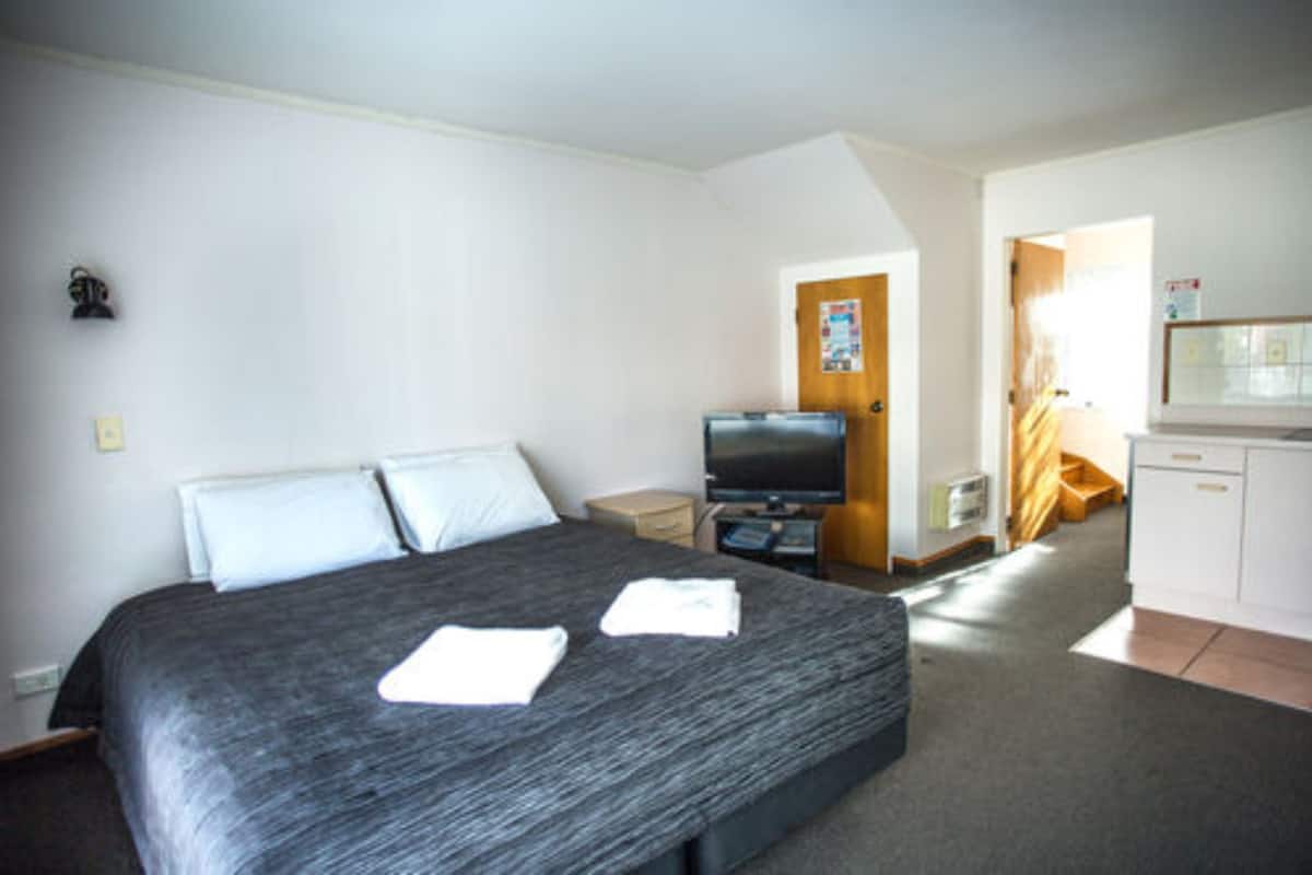 A hotel room with a large bed, a television, a desk, and a kitchenette.